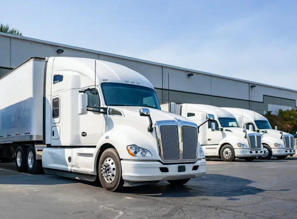White semi-trucks parked outside industrial building.